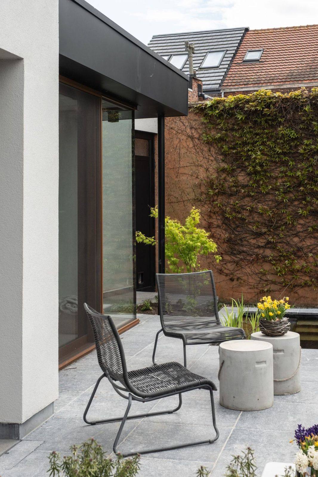 Totaalrenovatie van een stadstuin met natuursteen terras, strakke vijver en lounge stoelen