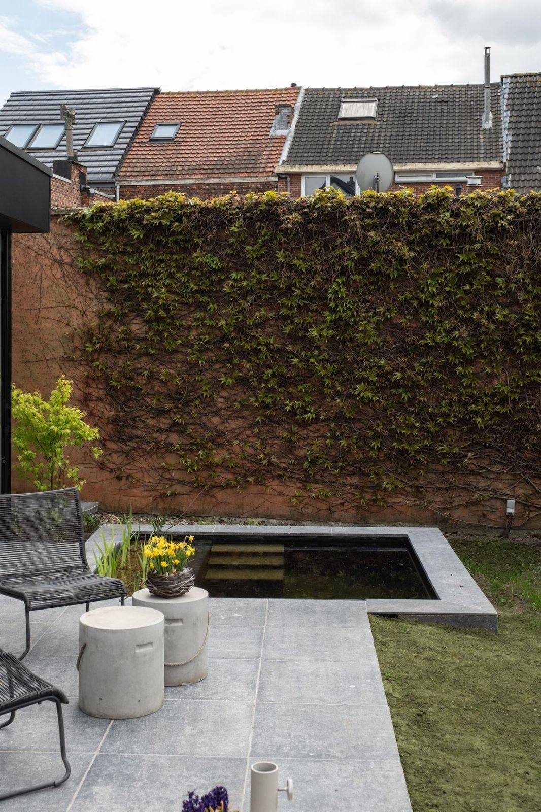 Stadstuin met strakke spiegelvijver, natuursteen terras en wijnrood begroeide muur
